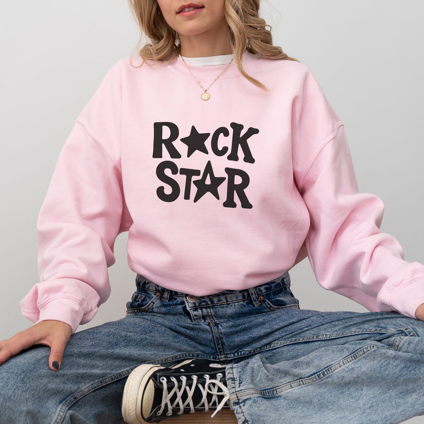 A woman wearing a pink sweatshirt with the text "ROCK STAR" printed on it, sitting cross-legged on the floor with her legs crossed.