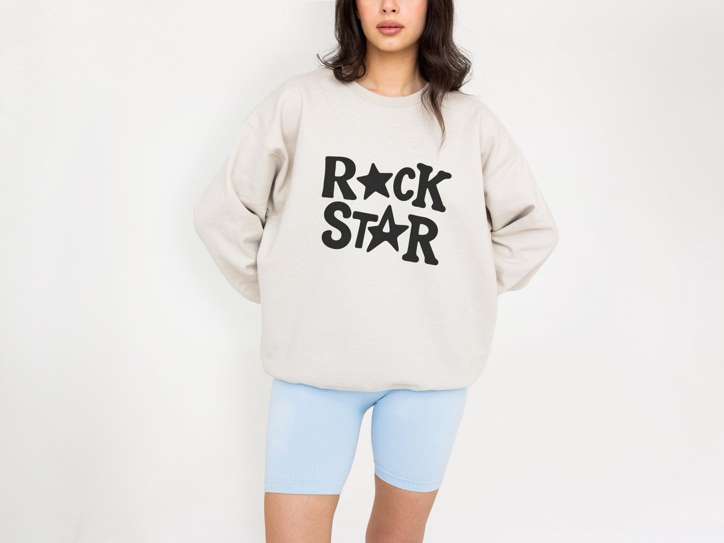 A woman wearing a beige sweatshirt with the text "ROCK STAR" printed on it.